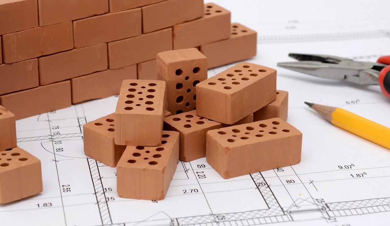 Small pieces of brick, a pair of pliers and a yellow pencil sitting on top of paper with illustrations on it
