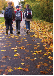 Children walking along the autumn leaved pavement to school